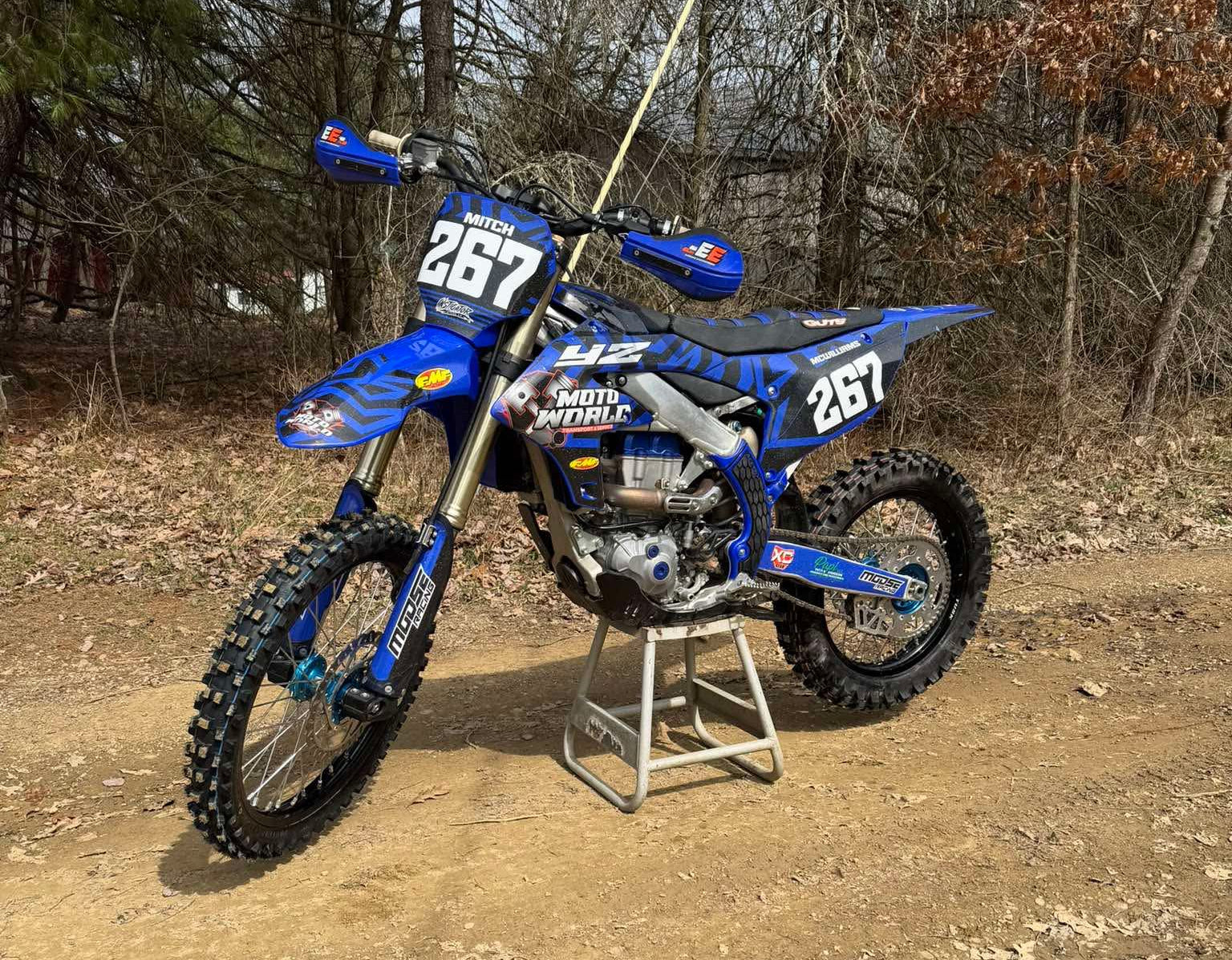 Blue dirt bike with number 267 on a stand in a wooded area